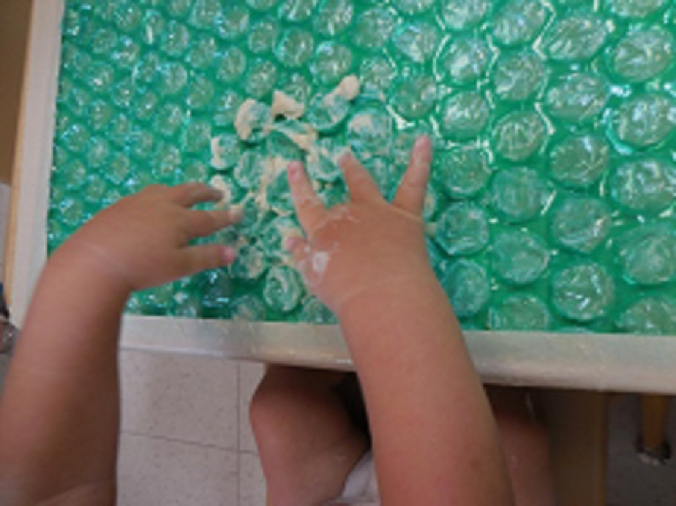 Baby sitting at a table playing with pudding on top of bubble wrap