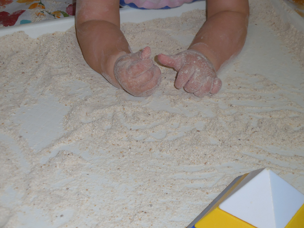 Small toddler on the floor playing with Matzah meal on a large tray as a tactile stimulus
