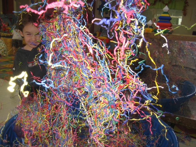 Preschool child throwing paper streamers into the air from a small kiddie pool filled with streamers
