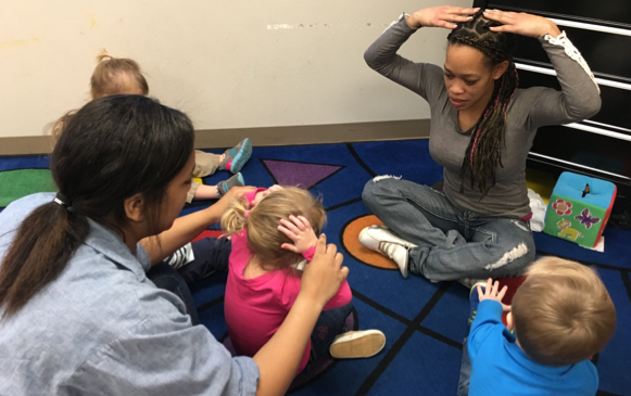 Two teachers on the floow using physical prompting with three toddlers