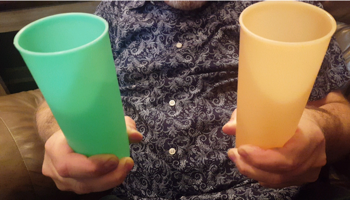 An adult holding a green platic cup on one hand and a yellow plastic cup in the other hand