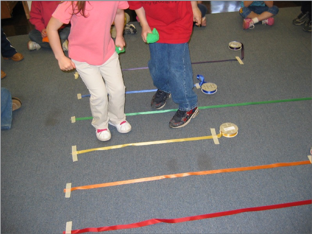 Two children standing with colored ribbons taped to the floor