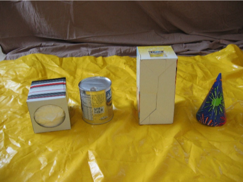 A kleenex box, paint can, empty box, and paper party hat placed on a tarp on the floor