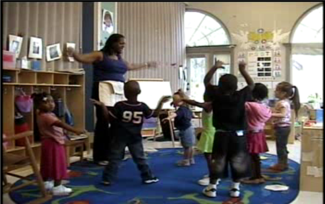 Children standing with the teacher pretending to be airplanes in the preschool classroom