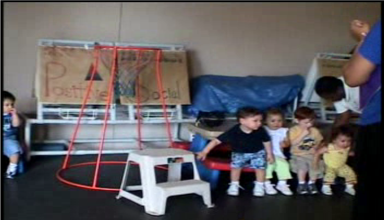 Small children sitting on the bench of a plastic picnic table in the preschool classroom