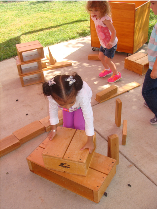 Two children playing outside with large wooden building blocks