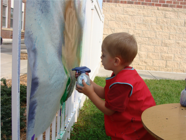 Boy spray painting outside on a piece of large paper hung on a fence