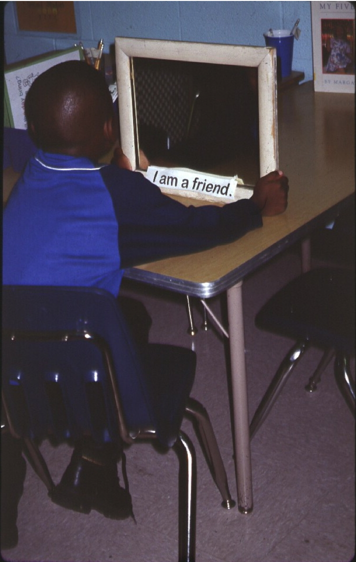 Child affirmation exercise in front of mirror with an I am a friend sticker on the mirror