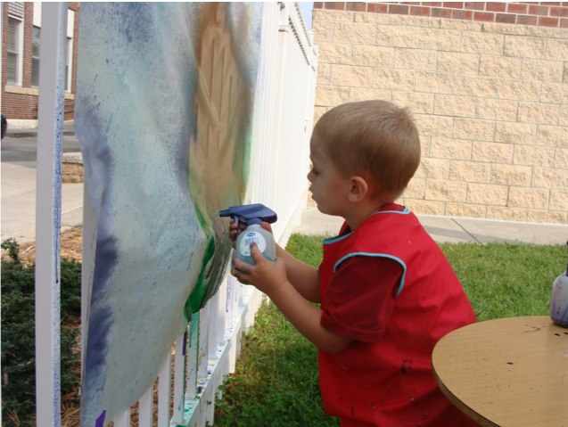 Boy with spray bottle painting a sheet outside